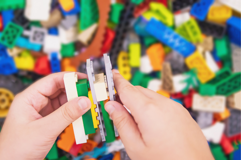A child's hands putting together Legos against a background of Legos