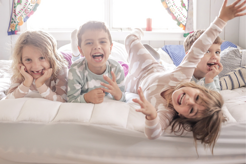 Four children in pajamas playing on a bed
