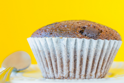 A large cupcake and spoon against a yellow background