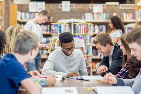 A group of teens talking and studying at a library