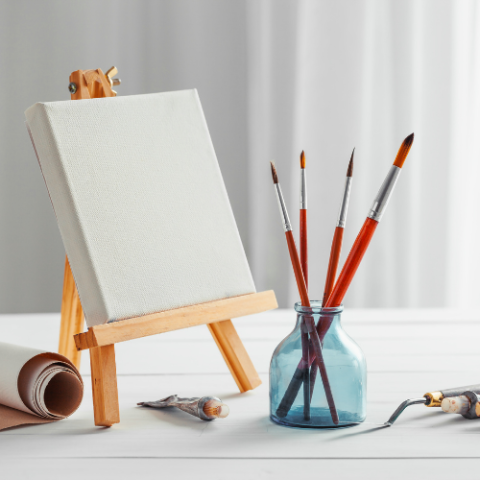 A small canvas on an easel next to a jar of paintbrushes