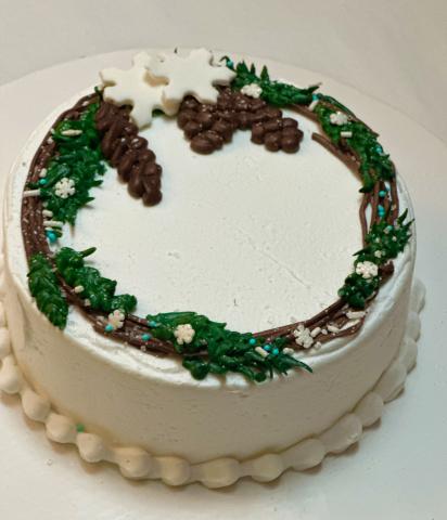 white cake with evergreen wreath, snowflake, and pinecone decorations