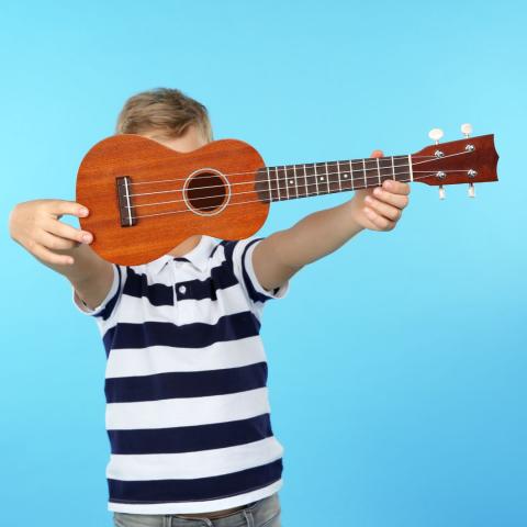 Photo image of child holding a ukulele with a blue background.