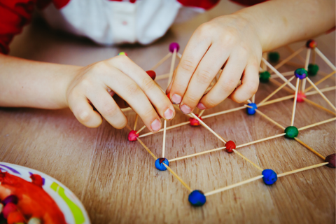 A child's hands putting together wooden dowels and play doh