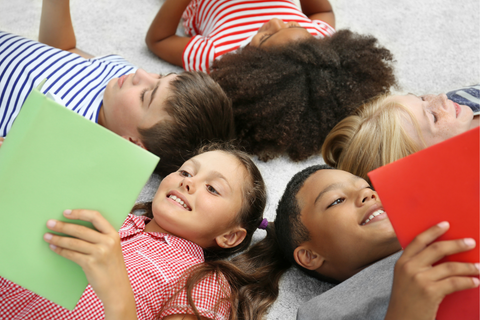 Children lie in a circle on the ground reading books