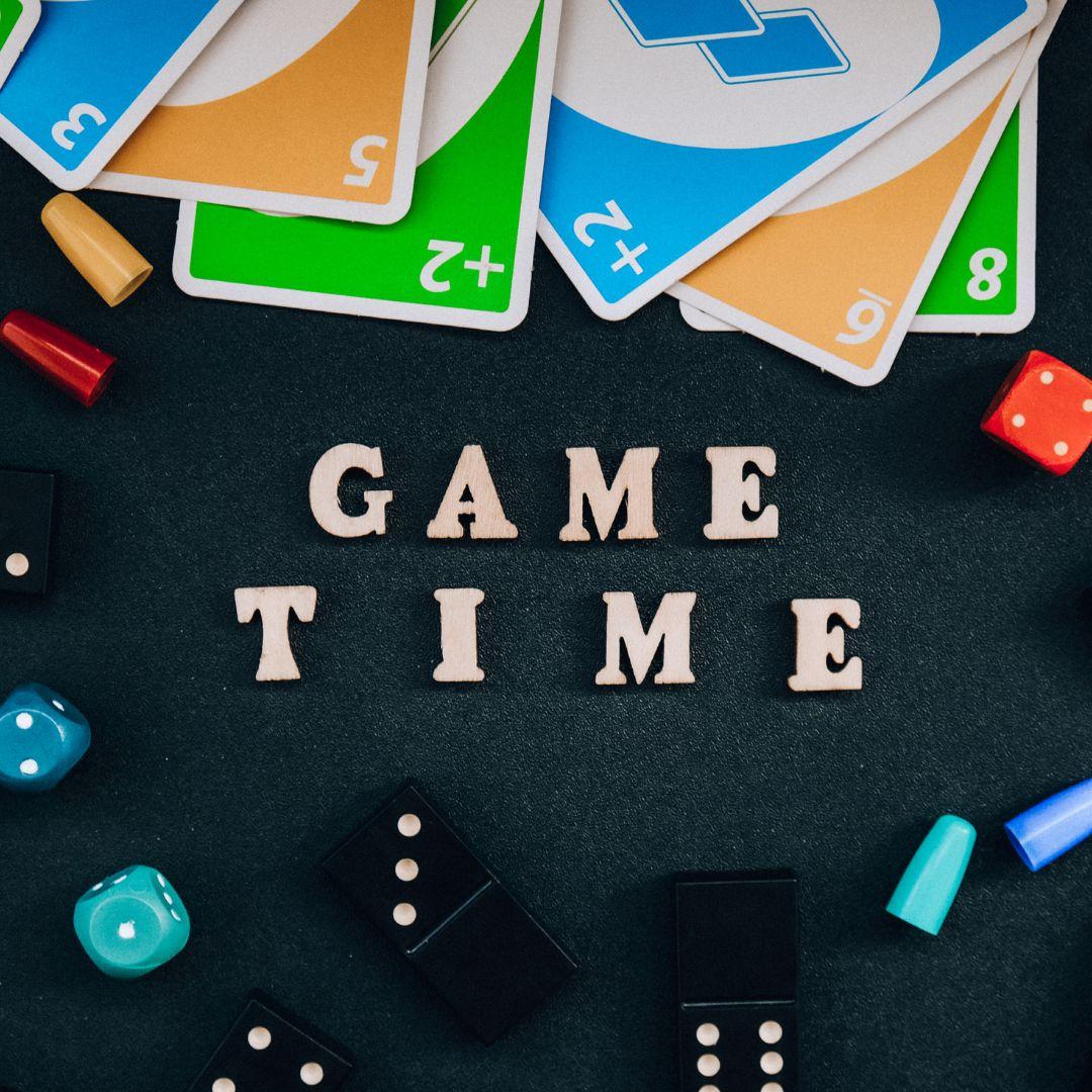 Black background with various game pieces and cards with white text reading Game Time