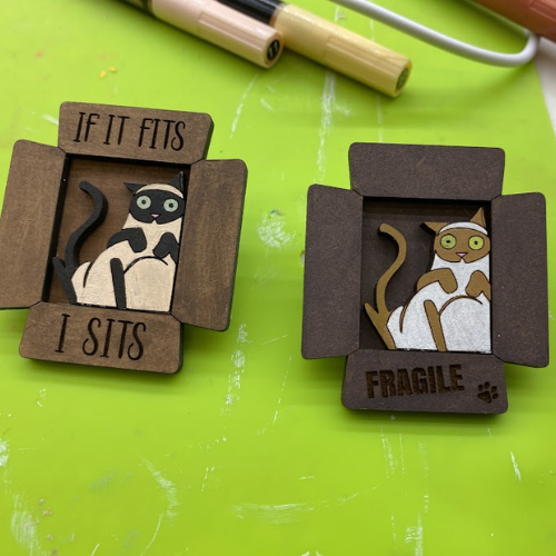 two wooden pins with cats on them sitting on a green surface